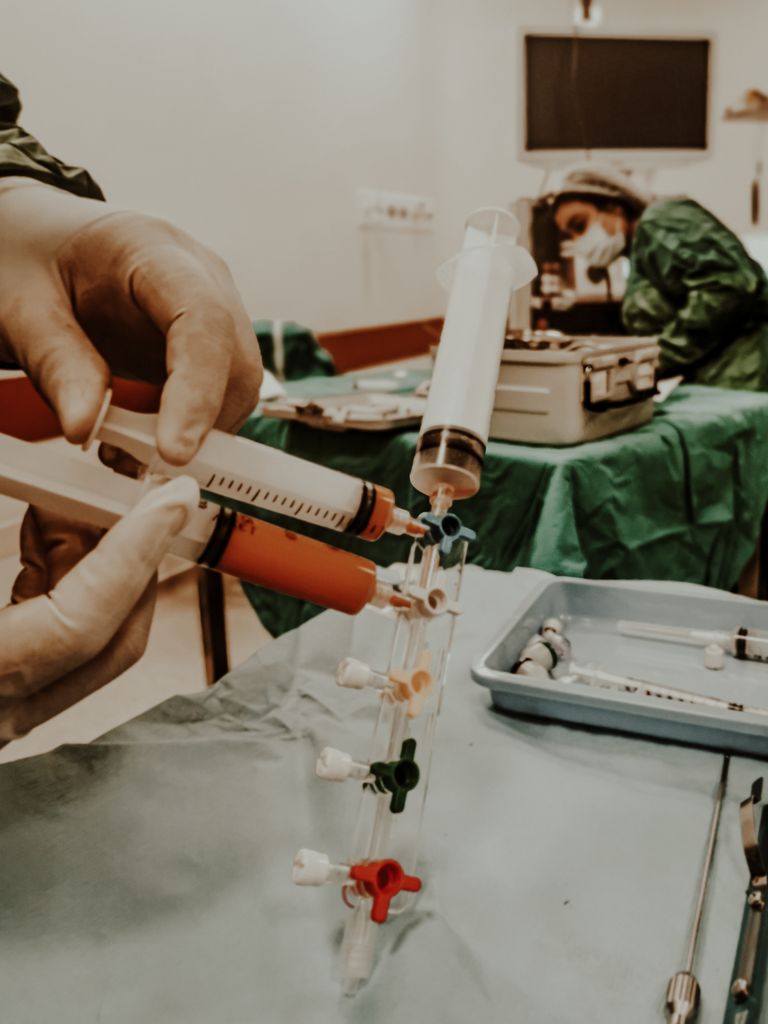 Surgeons setting up syringes and surgical tools for operation. Focus on hands and equipment.